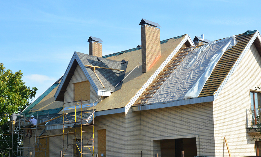 A roofer working on scaffolding while repairing the roof of a brick house under construction.